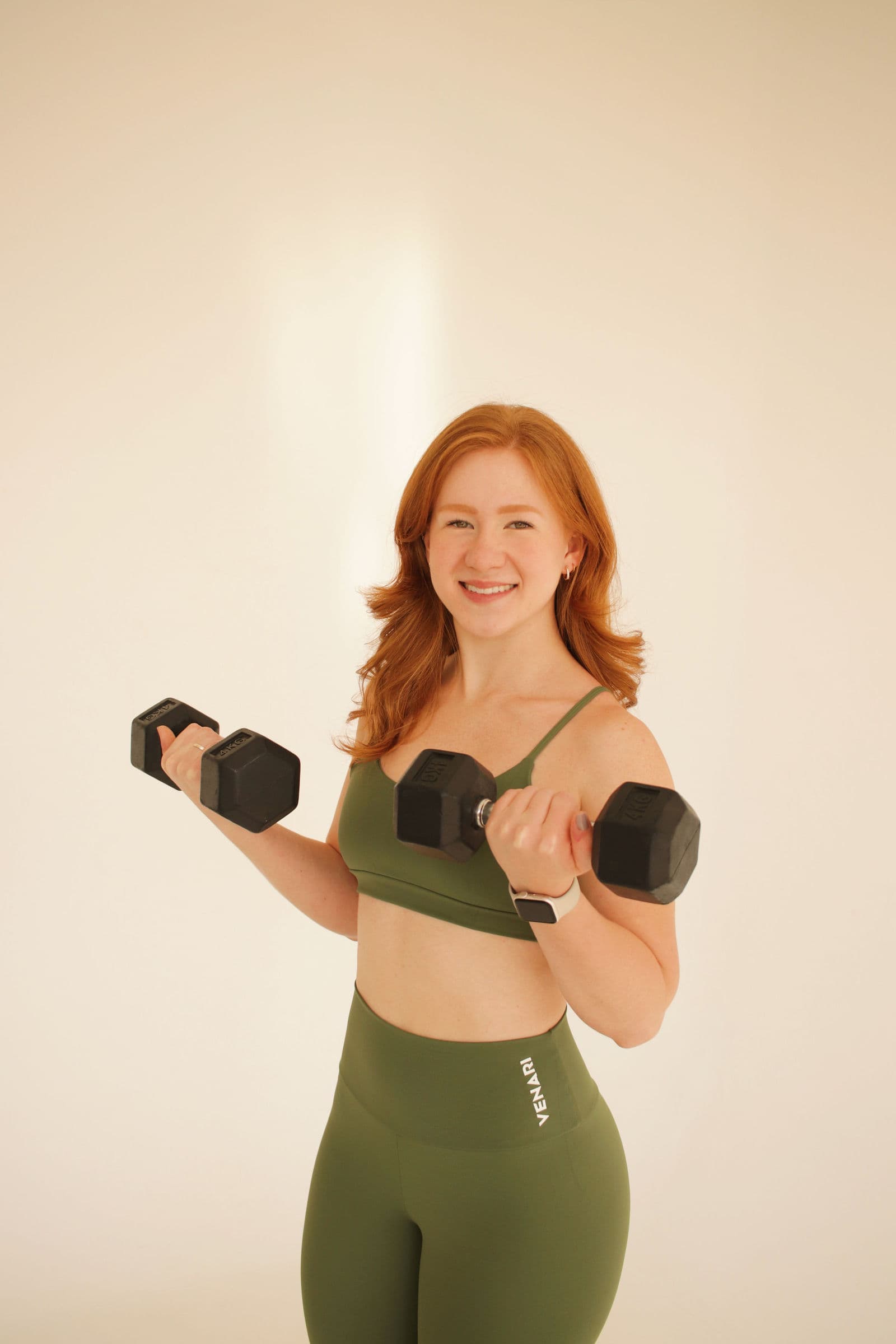 Natalie sorrindo fazendo rosca com halter, de conjunto verde